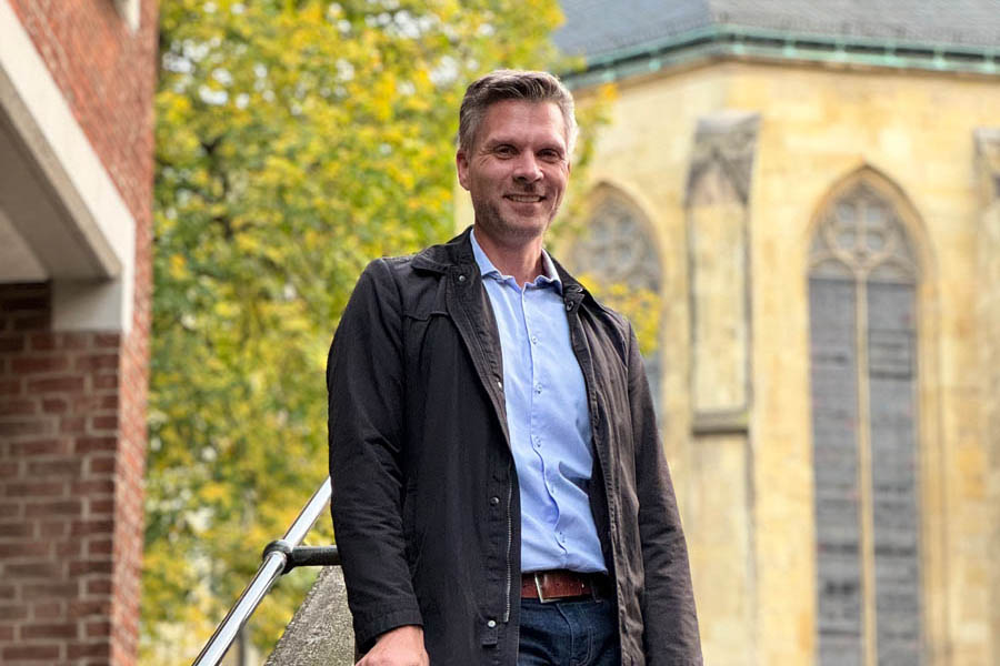 Auf dem Bild sieht man einen Mann auf einer Treppe vor einer Kirche stehen. Sein Name ist Ingo Fennen. Er ist der Geschäftsführer von Hörwerk Hörakustik. Er betreibt mit seinem Team aus Hörgeräteakustikern drei Standorte in Münster-Gremmendorf, Everswinkel und Ennigerloh.
